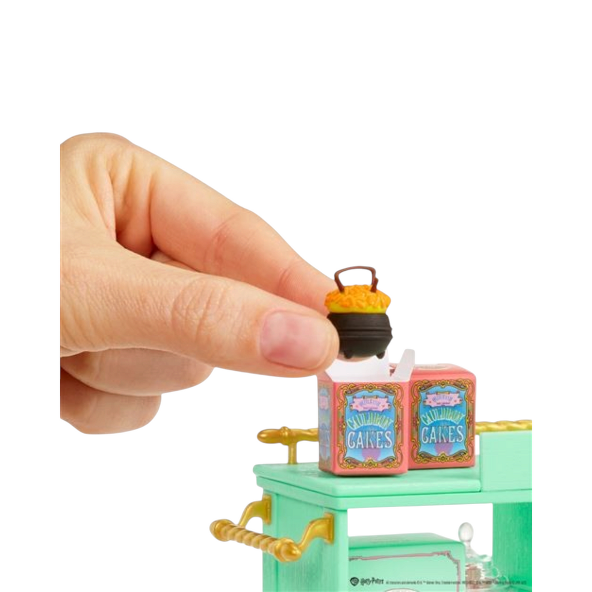 Main tenant une miniature de chaudron Honeydukes au-dessus d'un chariot La boutique Aux 2 Balais Harry Potter