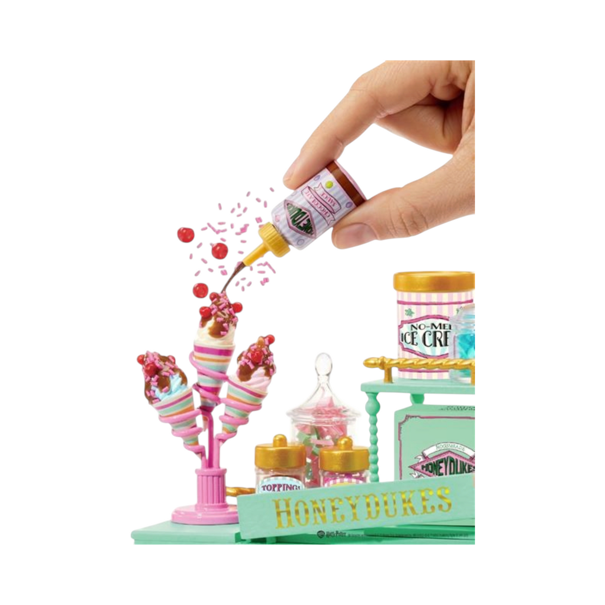Main de personne décorant des glaces miniatures avec de la sauce chocolat dans le set La boutique Aux 2 Balais Honeydukes