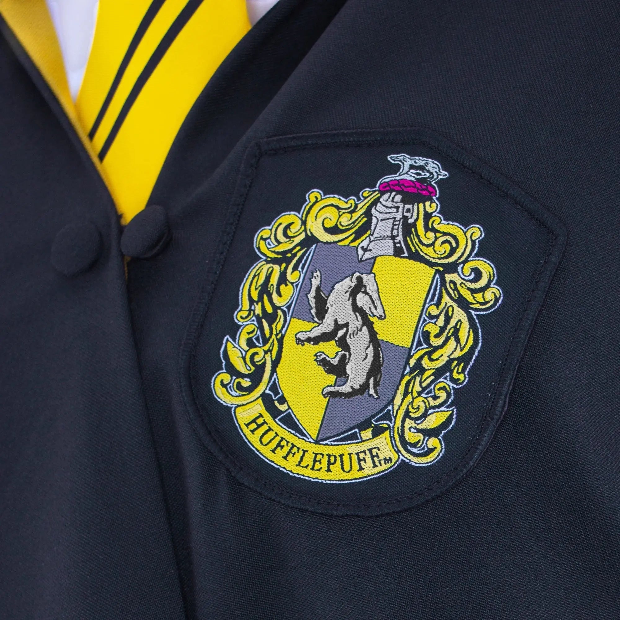 Robe de sorcier Hufflepuff bleu marine pour adulte en polyester, avec écusson brodé et cravate jaune rayée. La boutique Aux 2 Balais.